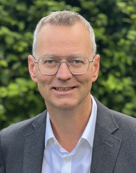 Portraitaufnahme zeigt Dr. Christian Kläne. Im Hintergrund unscharf eine grüne Hecke.